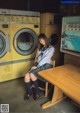 A woman sitting at a table in front of a washing machine.