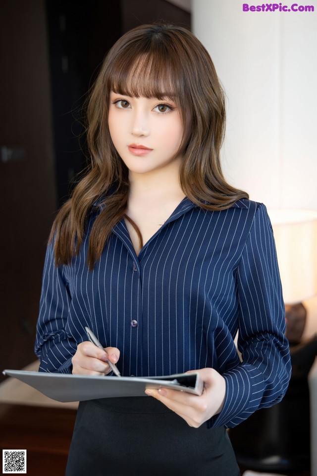 A woman in a blue shirt and black skirt holding a clipboard.