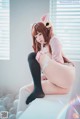 A woman in a pink shirt and black stockings sitting on a white table.