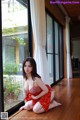 A woman in a red dress sitting on the floor by a window.