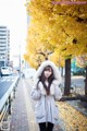 A woman in a gray coat is standing on a sidewalk.