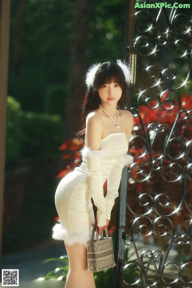 A woman in a white dress posing in front of a gate.
